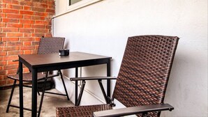 Een terras met een tafel en twee rieten stoelen, een bakstenen muur en een raam.