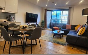 Ein modernes Wohnzimmer mit Essbereich, einer Couch, einem Couchtisch und einem Fernseher.