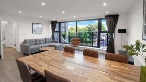 Een moderne kamer met een grote houten tafel, een grijze bank en een balkon met uitzicht.