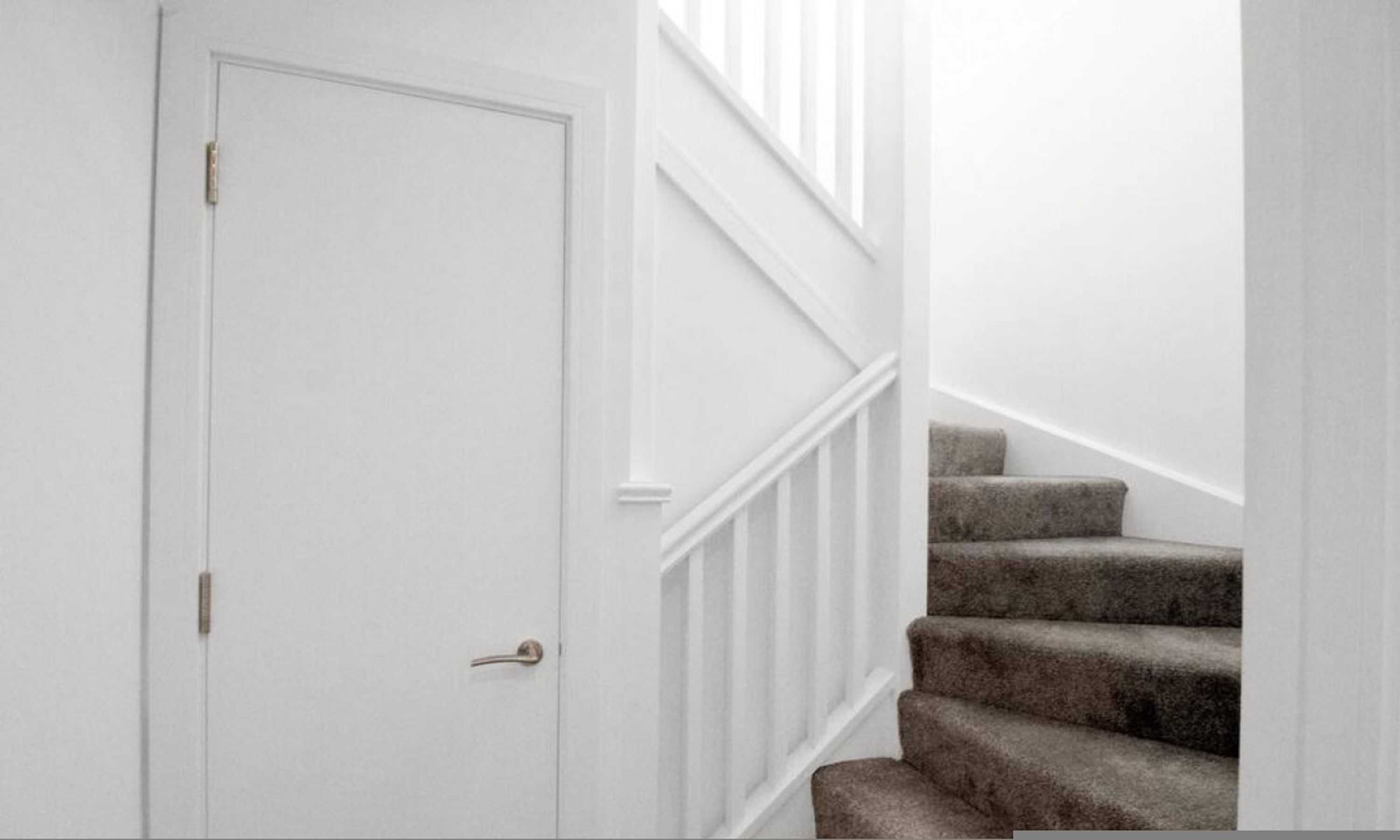 A white door with a brass handle, a staircase with a white railing, and carpeted steps.