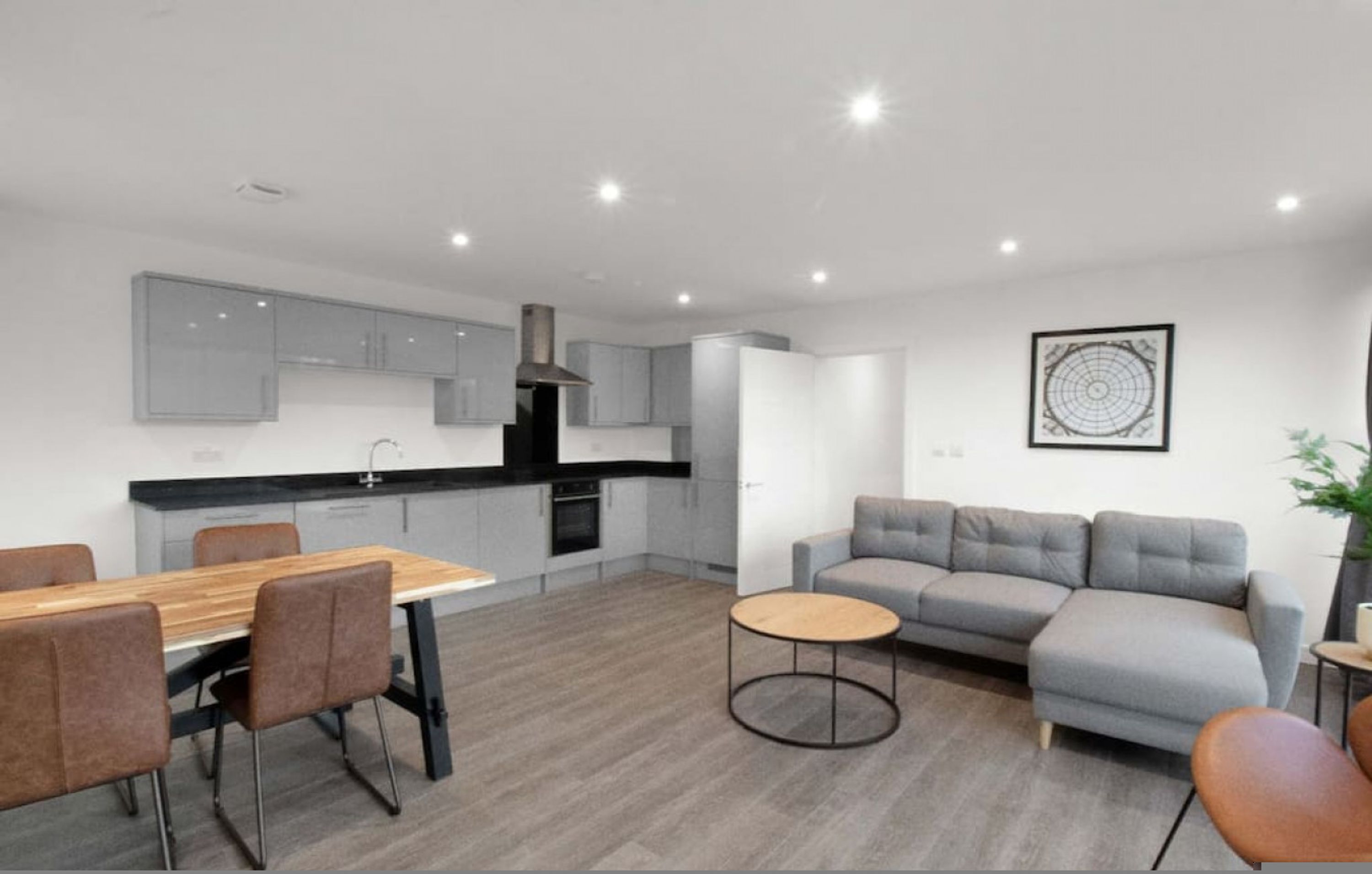A modern kitchen with grey cabinets, a dining table with chairs, a grey sofa, and a small round table.