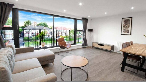 Een moderne woonkamer met een bank, ronde tafel, eettafel en stoelen. Grote ramen bieden uitzicht op het omliggende landschap.
