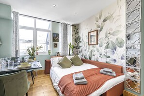 A hotel room with a bed, a dining table, a window, and a decorative wall. - Elegant 2bed Apt in the Heart of Covent Garden (London)