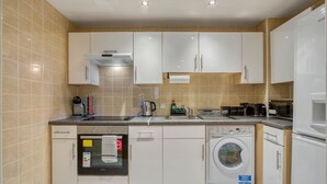 A modern kitchen with white cabinets, a built-in oven, a washing machine, and a coffee maker. - 1 Bed 1 Bath Next to Vauxhall Station - Zone 1 (London)
