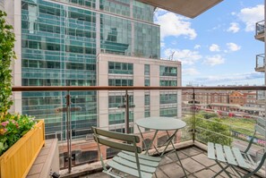 A balcony with a view of a modern building, a small round table, and a bench. - 1 Bed 1 Bath Next to Vauxhall Station - Zone 1 (London)