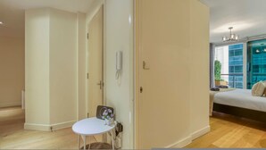 A modern bedroom with a bed, a small table with flowers, a bedside lamp, and a view of the outside through a window. - 1 Bed 1 Bath Next to Vauxhall Station - Zone 1 (London)
