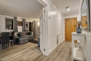 A living room with a sofa, dining table, and chairs, a wooden floor, and a door leading to another room. - Central Lux 4bed 3bath Penthouse (London)