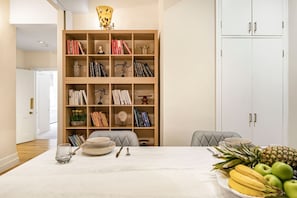 Ein Essbereich mit einem für zwei Personen gedecktem Tisch, einer Bücherwand mit Büchern und Dekoration sowie einem weißen Schrank mit Türen.