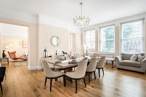 Uma sala de jantar com mesa posta para seis pessoas, um candelabro e grandes janelas com vista para a cidade.