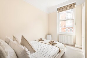 Ein Schlafzimmer mit Bett, Kissen, Heizkörper und einem Fenster mit Jalousien.
