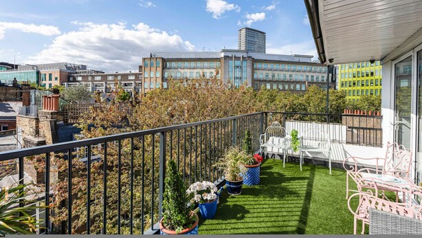 Un balcón con vistas a edificios, plantas en macetas y mobiliario de exterior.