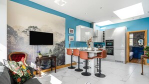 Una cocina moderna con armarios blancos, una zona de comedor con taburetes de bar y un televisor montado en la pared.