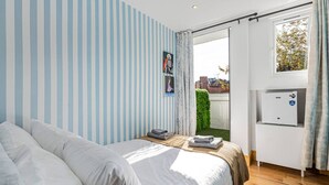 Un dormitorio con cama, una mesita con toallas, un calentador y una ventana con cortinas.