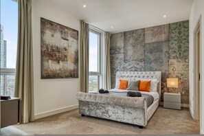 A bedroom with a large bed, a nightstand, a window, and a cityscape view. - Modern Penthouse in Nine Elms (London)