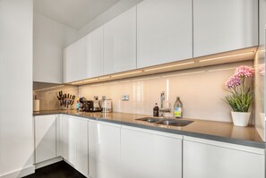 A modern kitchen with white cabinets, a stainless steel sink, and a countertop with various kitchen items. - Modern Penthouse in Nine Elms (London)