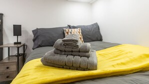 A neatly made bed with a yellow blanket and a stack of folded towels. - Studio in Central Reading- Next to Town Centre (Reading)
