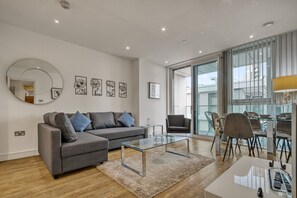 Ein modernes Wohnzimmer mit einem grauen Sofa, einem Glastisch und einem Essbereich mit Stühlen und einem Tisch.