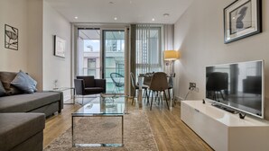 A modern living room with a sofa, coffee table, TV, and dining area. - 1 Bed Sofa Bed- Nine Elms Station - Zone 1 (London)