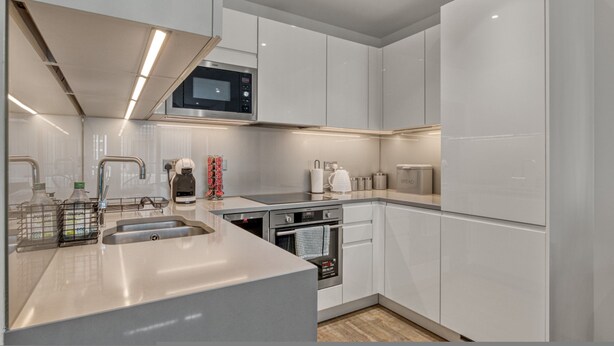A modern kitchen with white cabinetry, a microwave, a built-in oven, and a stainless steel sink. - 1 Bed Sofa Bed- Nine Elms Station - Zone 1 (London)