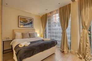 A hotel room with a bed, a nightstand, a framed artwork, and a large window with curtains. - Luxe Riverside Manhattan Studio (London)