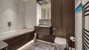 A modern bathroom with a bathtub, toilet, and sink. - Luxe Riverside Manhattan Studio (London)