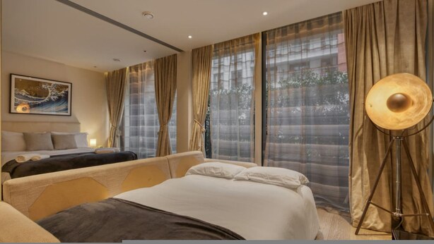 A hotel room with a bed, a bedside table, a lamp, and a painting on the wall. - Luxe Riverside Manhattan Studio (London)