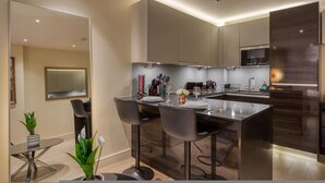 A modern kitchen with a central island, bar stools, and a dining table set for four. - Luxe Riverside Manhattan Studio (London)