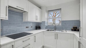 Une cuisine moderne avec des meubles blancs, une plaque de cuisson noire et une fenêtre équipée de stores.