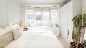 Un dormitorio con dos camas, un ventanal con cortinas, un ventilador de techo y una planta en maceta.