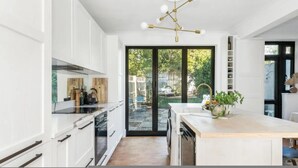 Una cocina moderna con armarios blancos, una isla central, horno empotrado y un ventanal con vistas a un jardín.