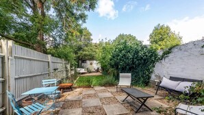 Un patio trasero con zona de estar, una silla blanca, una mesa y un sofá.