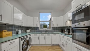 Eine moderne Küche mit weißen Schränken, einer integrierten Waschmaschine, einem großen Backofen und einem Fenster mit Blick auf Bäume.