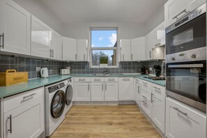 A modern kitchen with white cabinets, a built-in washing machine, a large oven, and a window with a view of trees. - Camden 2BR Gem Sleeps 5 Prime Location AC (London)