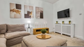 Ein Wohnzimmer mit einer Couch, einem Couchtisch mit Pflanze, einem Fernseher und Kunstwerken an der Wand.