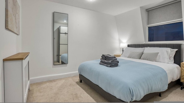 Ein Schlafzimmer mit Bett, Nachttisch, Spiegel und Fenster mit Blick.
