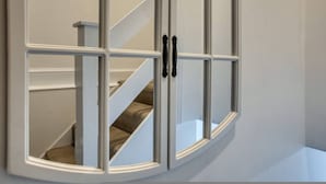 Eine Eckvitrine mit mehreren Glasscheiben und schwarzen Griffen.