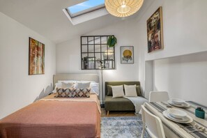 Quarto moderno com claraboia, cama, sofá, mesa de jantar e obras de arte nas paredes.