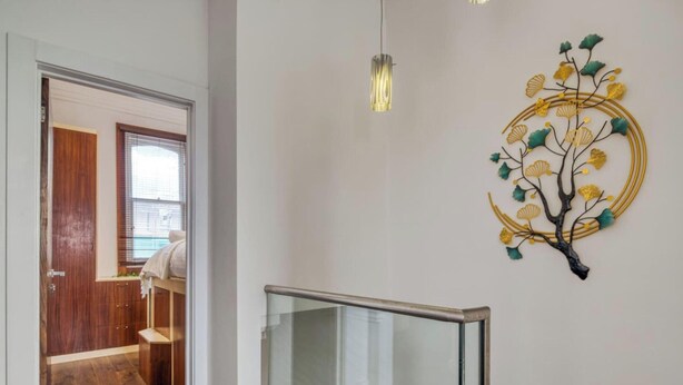 A hallway with a wooden door, a glass railing, and a wall-mounted decorative piece. - Mahogany Heights in Greater London (London)