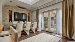 A modern living room with a flat-screen TV, a dining area with chairs, a fireplace, and a large sliding glass door to a balcony. - Mahogany Heights in Greater London (London)