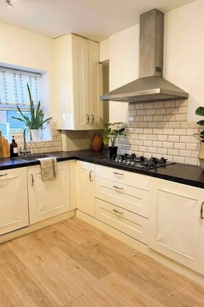A modern kitchen with white cabinets, a black countertop, and a stainless steel range hood. - Westbourne Park 3bdr Canal Side Home (London)