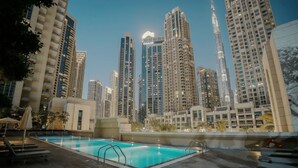 A rooftop pool with lounge chairs, surrounded by high-rise buildings and palm trees. - Prime Downtown Dubai 2-bed 2-bath With Parking (Dubai)