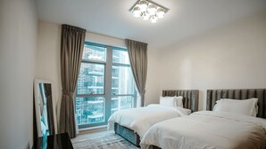 A hotel room with two beds, a large window with curtains, a modern light fixture, and a view of a cityscape. - Prime Downtown Dubai 2-bed 2-bath With Parking (Dubai)