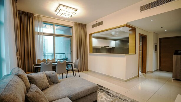 A modern living room with a sectional sofa, a dining area, and a kitchen visible through an open doorway. - Prime Downtown Dubai 2-bed 2-bath With Parking (Dubai)