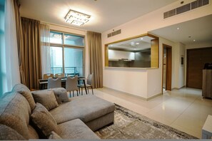 A modern living room with a sectional sofa, a dining area, and a kitchen visible through an open doorway. - Prime Downtown Dubai 2-bed 2-bath With Parking (Dubai)