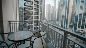 A balcony with a glass table and chairs, overlooking a cityscape with high-rise buildings. - Prime Downtown Dubai 2-bed 2-bath With Parking (Dubai)