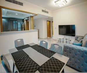 A modern living room with a dining area, a flat-screen TV, and a kitchen visible in the background. - Prime Downtown Dubai 2-bed 2-bath With Parking (Dubai)