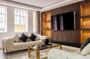 A modern living room with a white sofa, a glass coffee table, and a mounted TV. - Luxury 4 Bed Knightsbridge (London)