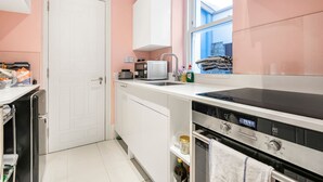 A kitchen with a white door, a window, a sink, a stove, and a dishwasher. - The Grand Camden Garden 5BR Home (London)