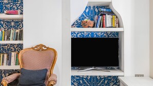 A room with a bookshelf, a television, and a patterned chair. - The Grand Camden Garden 5BR Home (London)