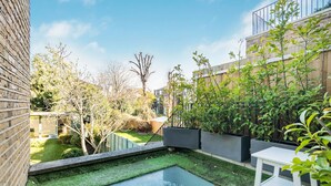 A courtyard with a small pool, potted plants, and a white table. - The Grand Camden Garden 5BR Home (London)